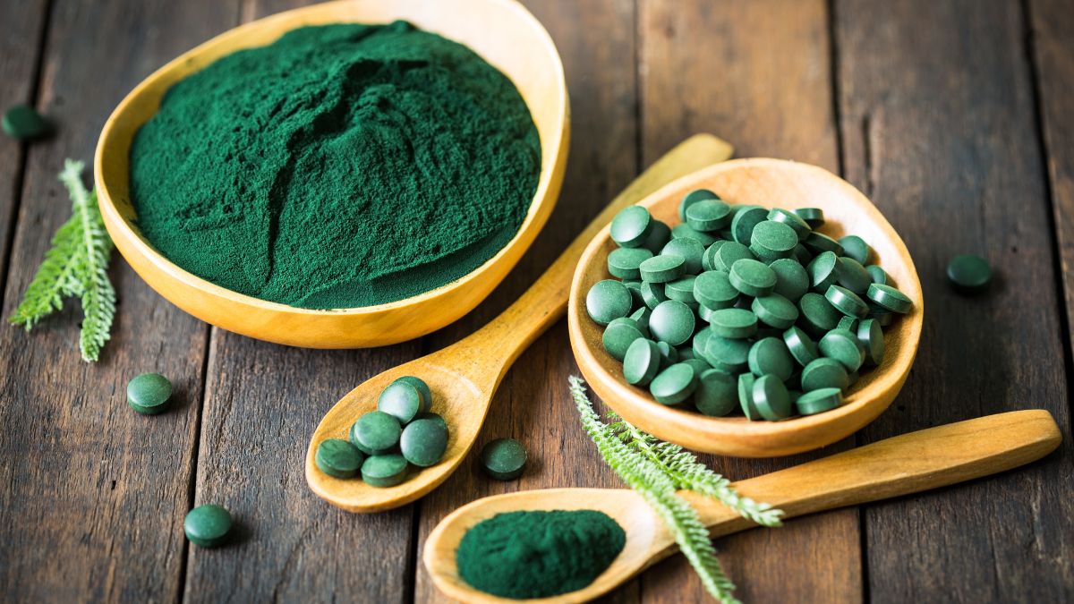 Zöld spirulina por és tabletták fából készült tálakban, friss zöld levelekkel.
