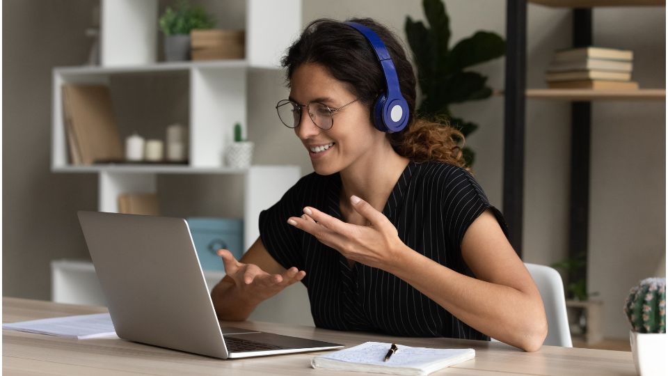 Egy fiatal nő vidáman beszélget a laptopján, fejhallgatóval.