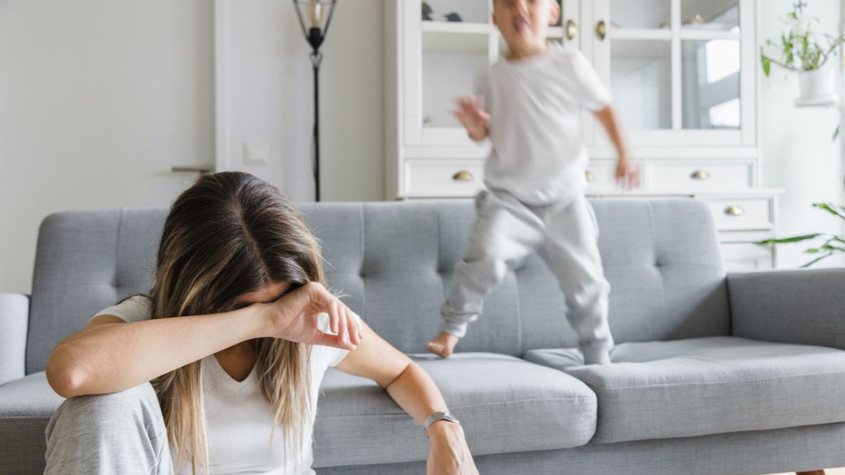 Egy fáradt anya ül a kanapén, míg a hiperaktív kisfiú ugrál mellette.