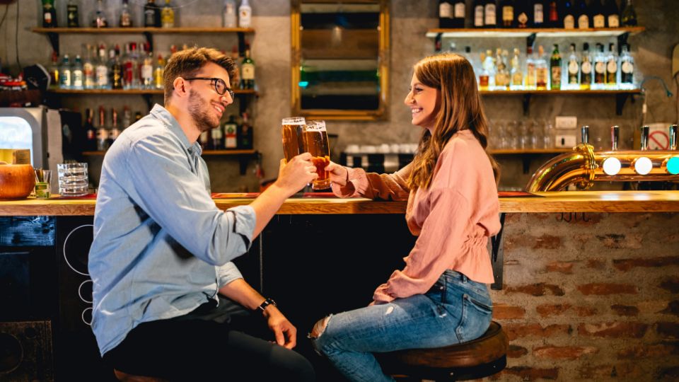 Egy fiatal pár koccint a bárpultnál, boldog és laza hangulatban.