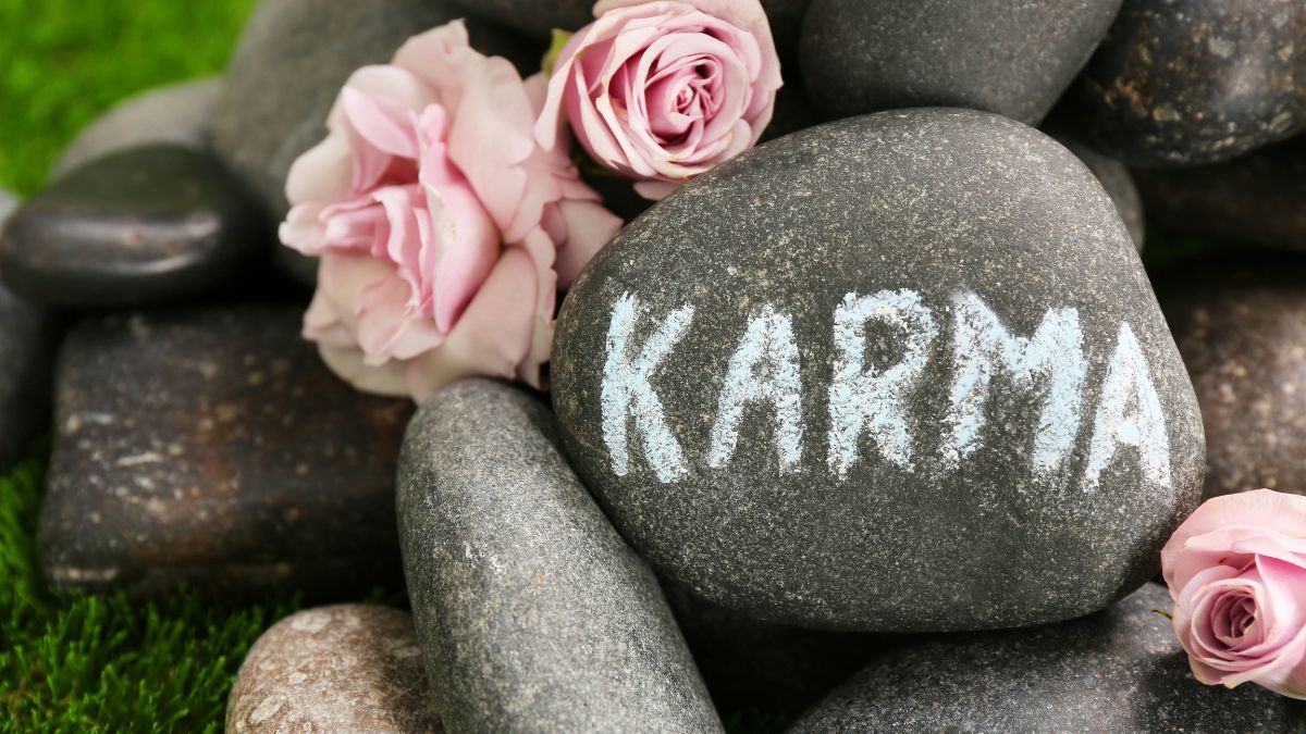 Kövek között elhelyezett virágokkal díszített kő, amelyen a 'KARMA' felirat látható.