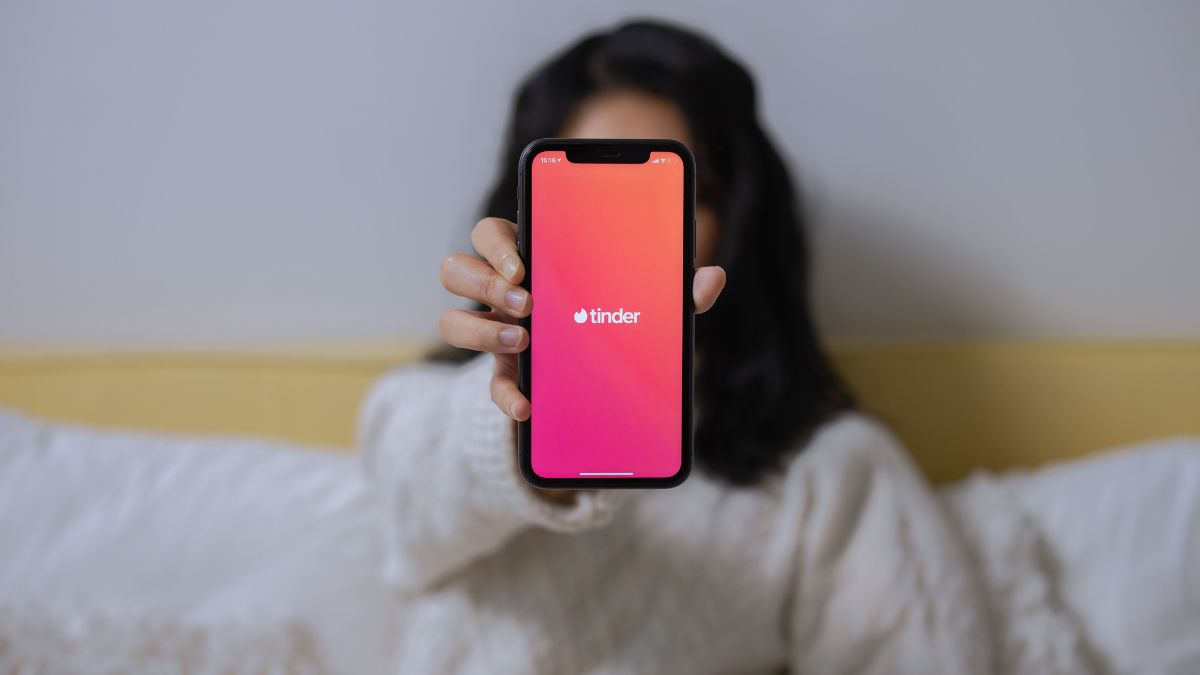 Egy fiatal nő a kezében tart egy okostelefont, amelyen a Tinder alkalmazás logója látható.