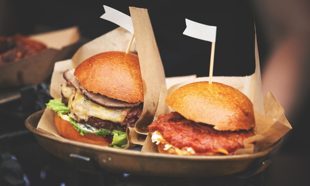 Két ízletes hamburger, friss zöldségekkel és különféle feltétekkel tálalva.